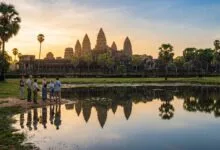 Sunrise view of Angkor Wat temple in Cambodia with a small group of visitors reflecting in the foreground pond