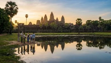 Sunrise view of Angkor Wat temple in Cambodia with a small group of visitors reflecting in the foreground pond