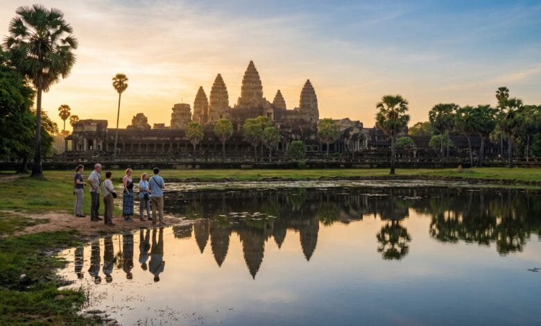 Sunrise view of Angkor Wat temple in Cambodia with a small group of visitors reflecting in the foreground pond