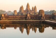 Angkor Wat temple in Cambodia at sunrise, with its five towers reflected in the moat and golden morning light illuminating the ancient stone.