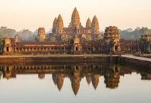 Angkor Wat temple in Cambodia at sunrise, with its five towers reflected in the moat and golden morning light illuminating the ancient stone.