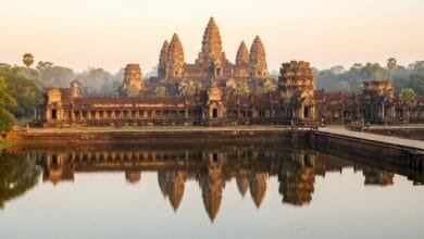 Angkor Wat temple in Cambodia at sunrise, with its five towers reflected in the moat and golden morning light illuminating the ancient stone.