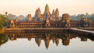 Angkor Wat temple in Cambodia at sunrise, with its five towers reflected in the moat and golden morning light illuminating the ancient stone.