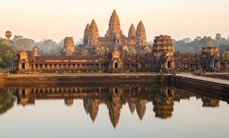 Angkor Wat temple in Cambodia at sunrise, with its five towers reflected in the moat and golden morning light illuminating the ancient stone.