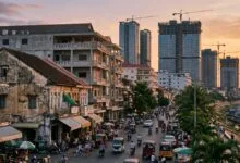 Phnom Penh cityscape at sunset with modern high-rise buildings under construction alongside older low-rise shophouses and busy street traffic
