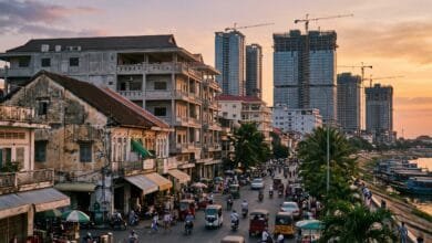 Phnom Penh cityscape at sunset with modern high-rise buildings under construction alongside older low-rise shophouses and busy street traffic