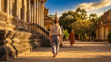 A traveler dressed modestly walks through a Cambodian temple grounds at golden hour with a monk in the background