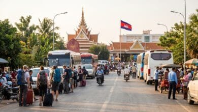 Travelers with luggage waiting near an immigration checkpoint at a Cambodia land border crossing