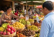 A vendor at a Cambodian market displays a QR code payment placard while a customer pays with a smartphone.
