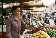 A market vendor in Phnom Penh holds a smartphone to accept a QR code payment from a customer at her stall