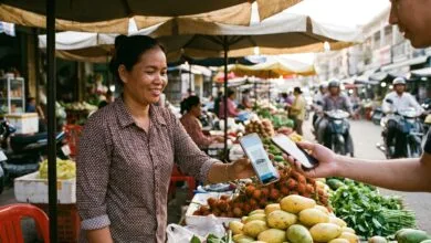 A market vendor in Phnom Penh holds a smartphone to accept a QR code payment from a customer at her stall