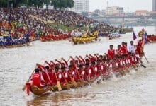 A long wooden racing boat with dozens of Khmer rowers paddling in unison on the Tonle Sap River during Cambodia's Water Festival