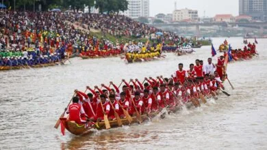 A long wooden racing boat with dozens of Khmer rowers paddling in unison on the Tonle Sap River during Cambodia's Water Festival