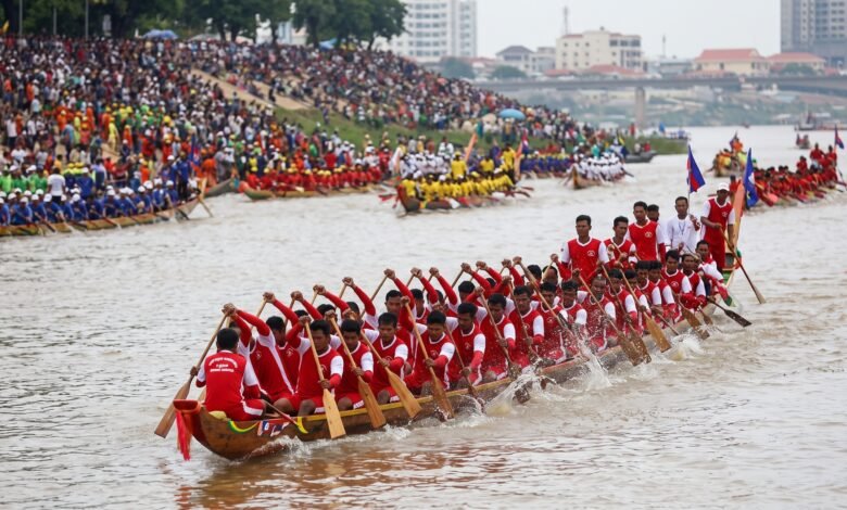 A long wooden racing boat with dozens of Khmer rowers paddling in unison on the Tonle Sap River during Cambodia's Water Festival