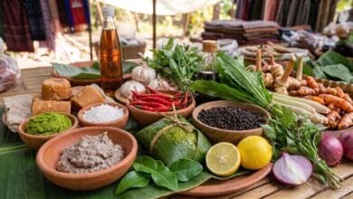 A woven bamboo mat displaying Cambodian cooking ingredients including prahok fish paste, kroeung paste, Kampot peppercorns, palm sugar, lemongrass, galangal, and turmeric