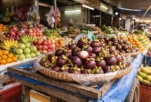 Fresh Cambodian mangosteen fruits with deep purple rinds and white segmented flesh inside, displayed in a bamboo basket at a market stall
