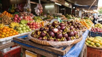 Fresh Cambodian mangosteen fruits with deep purple rinds and white segmented flesh inside, displayed in a bamboo basket at a market stall