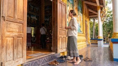 A traveler standing respectfully at the entrance of a Cambodian pagoda, shoes removed, looking toward the main hall
