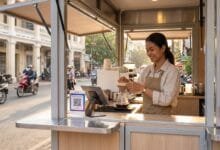 A young Cambodian woman entrepreneur prepares coffee at a modern kiosk on a Phnom Penh street