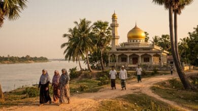 A mosque with a golden dome and minaret rising above palm trees near the Mekong River in Cambodia