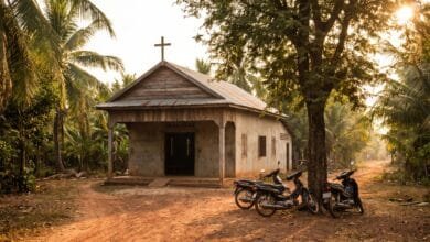 A small church building with a cross on the roof, surrounded by tropical vegetation in Cambodia