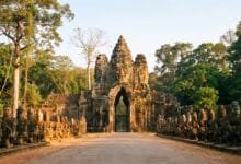 The South Gate of Angkor Thom with massive stone face towers and a causeway lined with god and demon statues.
