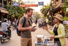 A foreign traveler smiles while talking with a Cambodian vendor at a street food stall in Siem Reap, holding a phrasebook.
