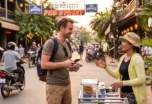 A foreign traveler smiles while talking with a Cambodian vendor at a street food stall in Siem Reap, holding a phrasebook.