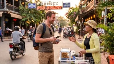 A foreign traveler smiles while talking with a Cambodian vendor at a street food stall in Siem Reap, holding a phrasebook.
