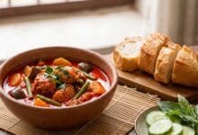 Traditional Khmer red curry in a ceramic bowl with chicken, eggplant, and long beans, served with sliced French baguette.
