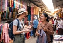 A foreign traveler smiling and speaking with a Cambodian market vendor at a clothes shop
