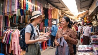 A foreign traveler smiling and speaking with a Cambodian market vendor at a clothes shop