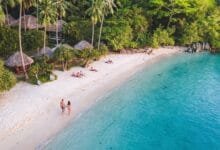Main beach on Koh Tonsay, Cambodia, with white sand, coconut palms, wooden bungalows, and calm shallow water