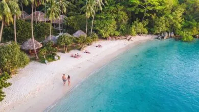 Main beach on Koh Tonsay, Cambodia, with white sand, coconut palms, wooden bungalows, and calm shallow water