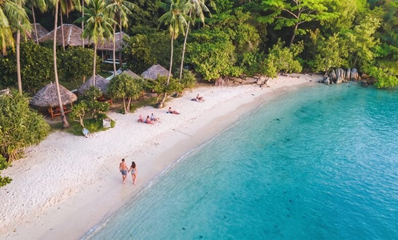 Main beach on Koh Tonsay, Cambodia, with white sand, coconut palms, wooden bungalows, and calm shallow water