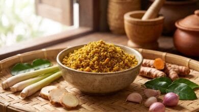 Golden-yellow Cambodian kroeung spice paste in a ceramic bowl surrounded by lemongrass, galangal, turmeric, and kaffir lime leaves.
