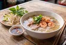 A bowl of Cambodian Kuy Teav rice noodle soup with pork, shrimp, and fresh herbs