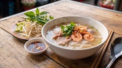 A bowl of Cambodian Kuy Teav rice noodle soup with pork, shrimp, and fresh herbs