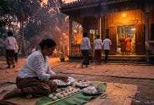 A Cambodian woman in traditional white clothing places sticky rice balls onto a banana leaf at a pagoda during Pchum Ben festival at dawn.