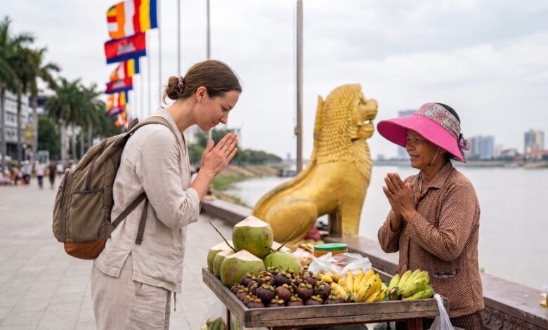 A foreign traveler presses their palms together in a sampeah gesture toward a smiling Cambodian vendor at a riverside stall near the Royal Palace in Phnom Penh.