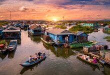 Wide view of a floating village on Tonlé Sap Lake in Cambodia at sunset, with stilt houses and small boats on the water