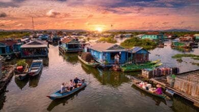 Wide view of a floating village on Tonlé Sap Lake in Cambodia at sunset, with stilt houses and small boats on the water