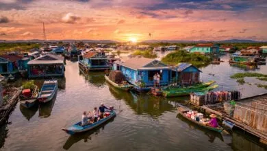 Wide view of a floating village on Tonlé Sap Lake in Cambodia at sunset, with stilt houses and small boats on the water