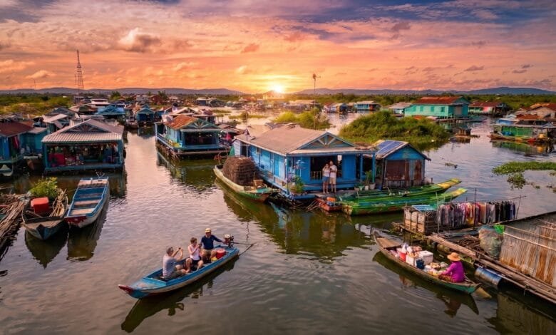 Wide view of a floating village on Tonlé Sap Lake in Cambodia at sunset, with stilt houses and small boats on the water