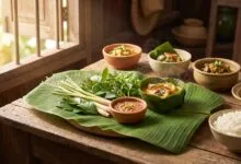Traditional Cambodian cuisine spread with fish amok in banana leaf, jasmine rice, prahok dipping sauce, and fresh herbs on a wooden table
