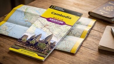 Folded National Geographic Cambodia Adventure Map 3024 travel map displayed on a wooden table beside a passport and small notebook.