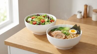Two DOWAN white porcelain serving bowls on a kitchen counter, one with salad and one with noodles.