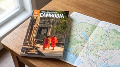 The Rough Guide to Cambodia 7th edition paperback travel guide resting on a wooden table with a colour map of Cambodia open beside it.